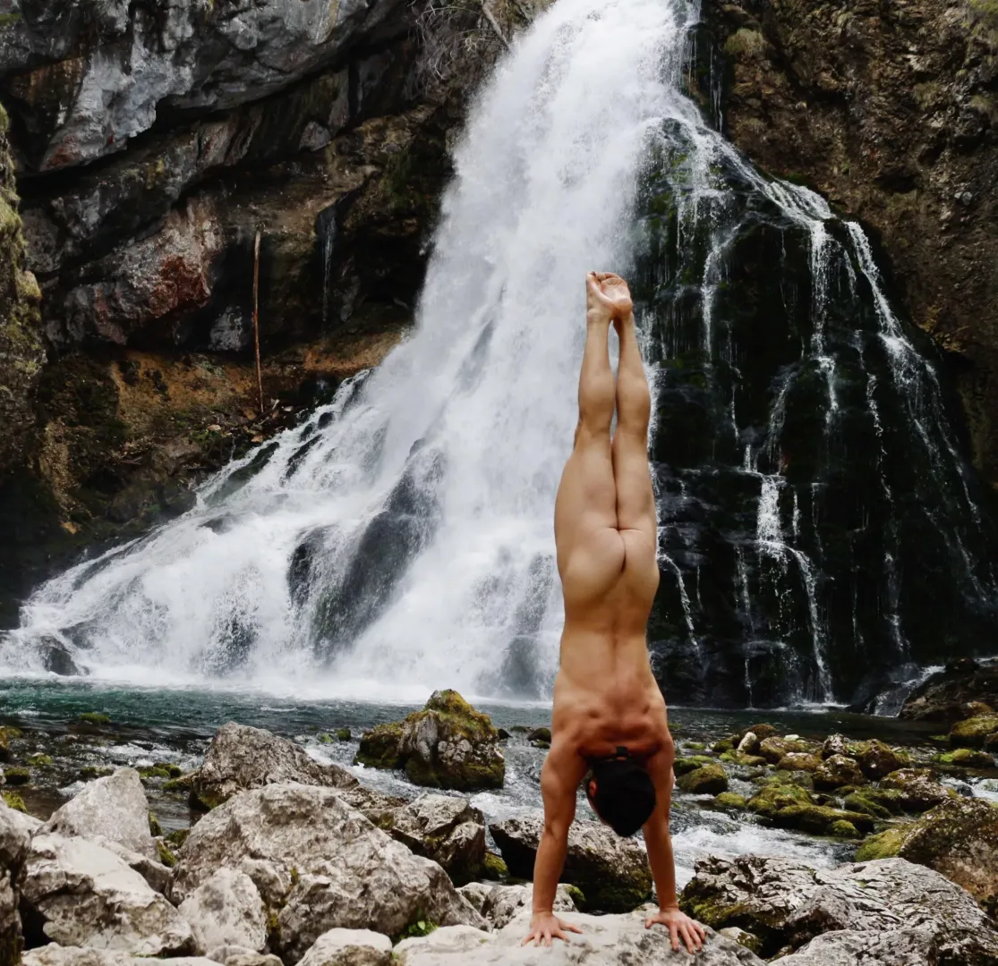 Naked Yoga handstand in nature front of waterfall